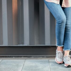 Stylish woman in jeans and glitter sneakers leans casually outdoors.