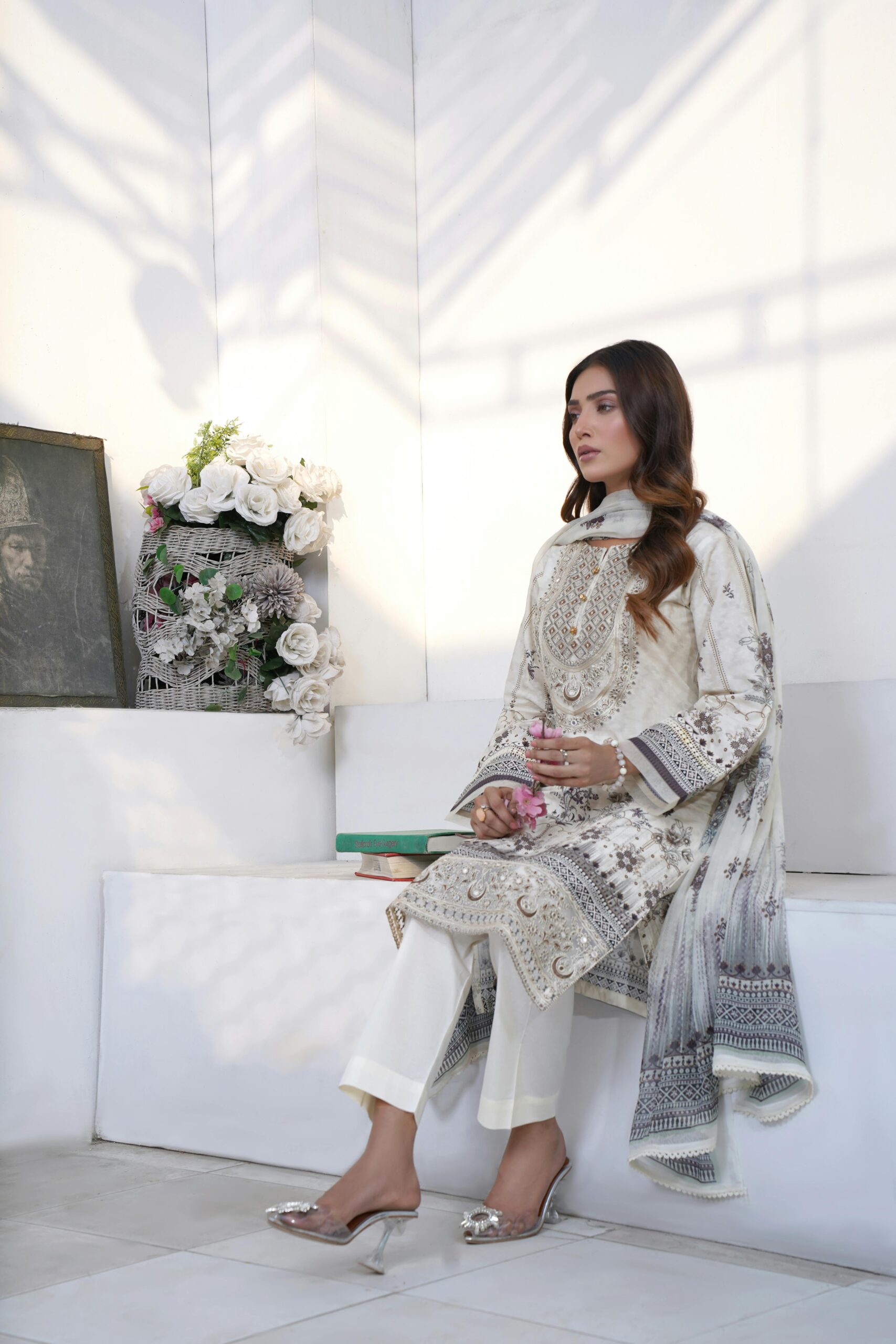 Woman in traditional Pakistani dress seated indoors, wearing a white embroidered outfit.